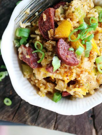 a white bowl filled with rice and sausage next to a fork on top of a wooden table