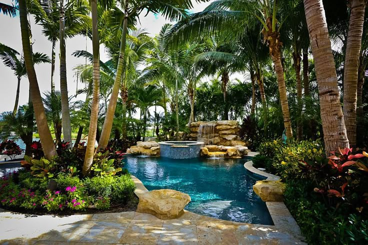 an outdoor swimming pool surrounded by palm trees and other tropical plants, with a waterfall in the middle