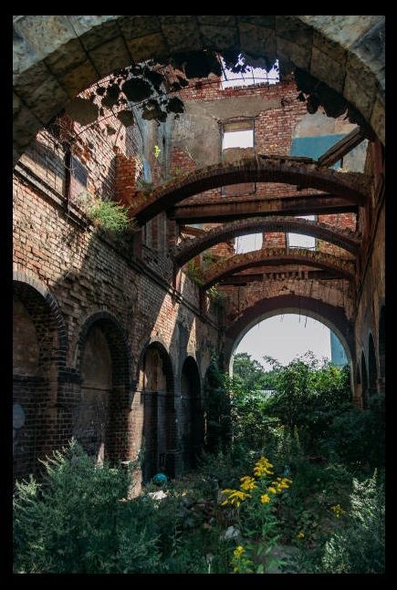 an old brick building with arches and flowers in the foreground, looking up into the sky