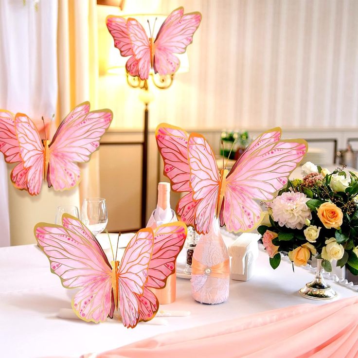 three pink butterflies sitting on top of a table next to bottles and vases filled with flowers