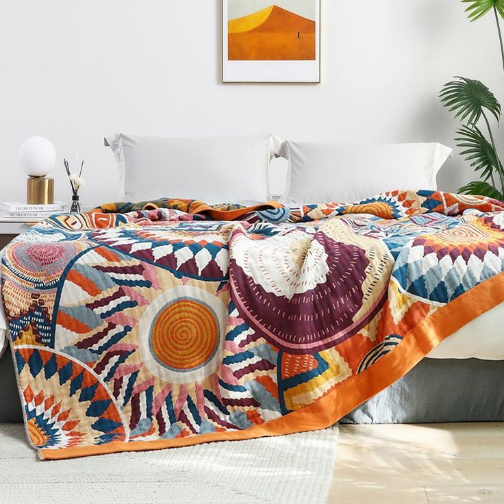 a bed with a colorful blanket on top of it next to a potted plant