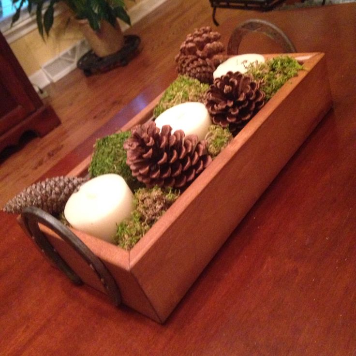 an arrangement of pine cones, moss and candles in a wooden box on a table