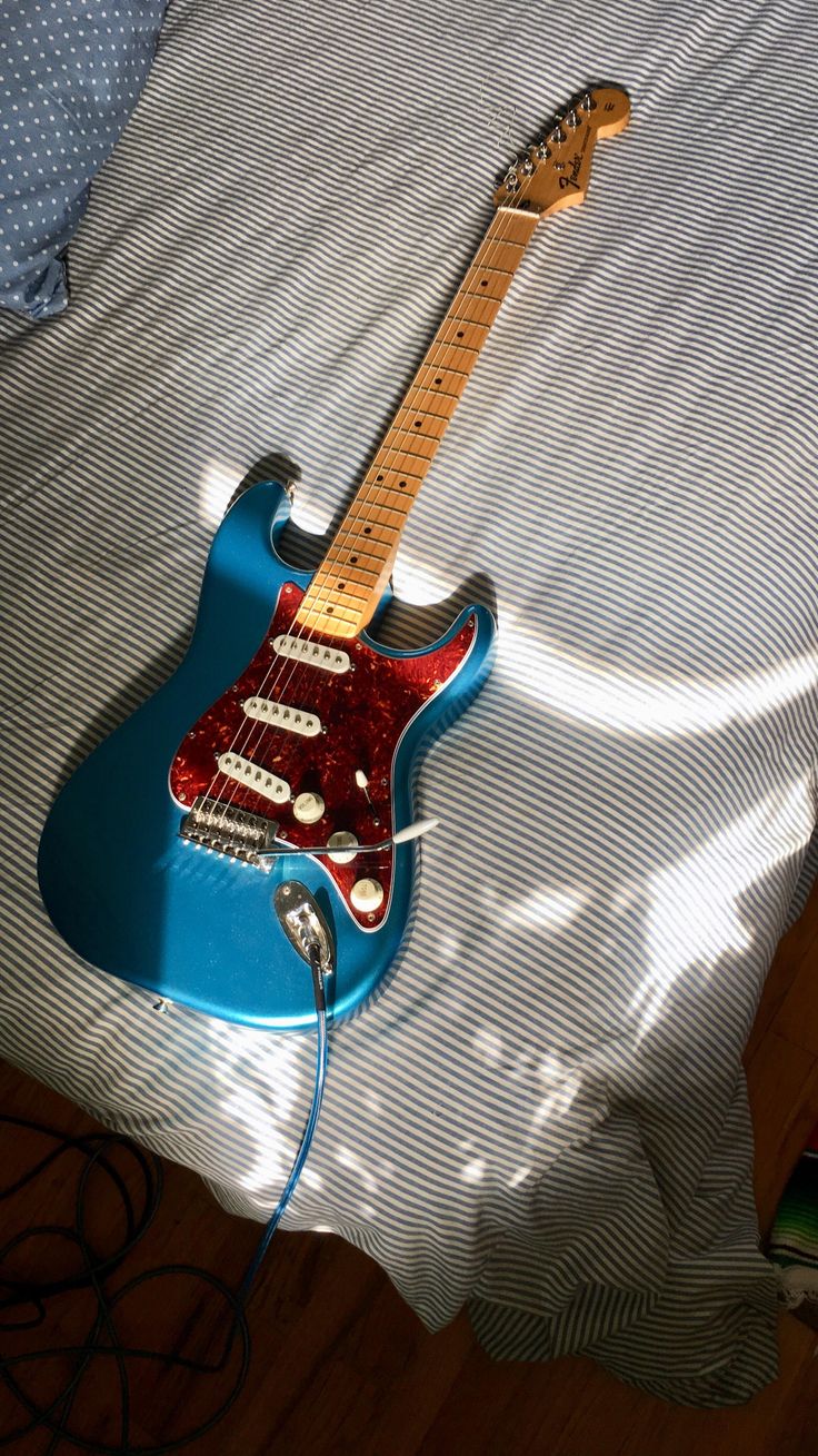 a blue electric guitar sitting on top of a bed