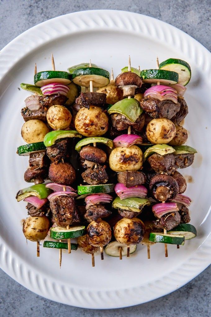 skewered meat and vegetables on a plate with toothpicks in the middle