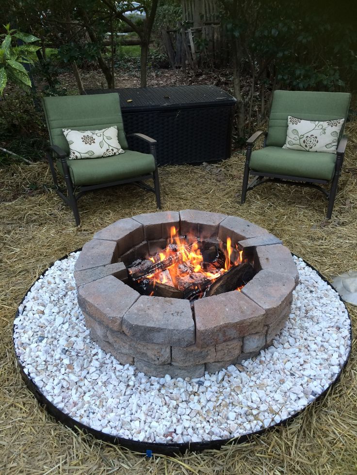 a fire pit sitting on top of a gravel covered field next to two lawn chairs