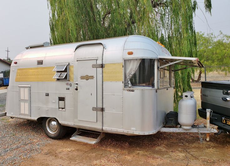 an old camper trailer parked next to a black car in a parking lot near a tree