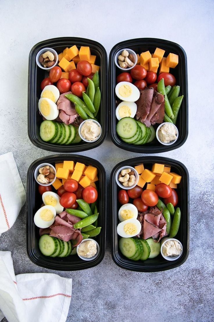 four black trays filled with different types of food on top of a gray table