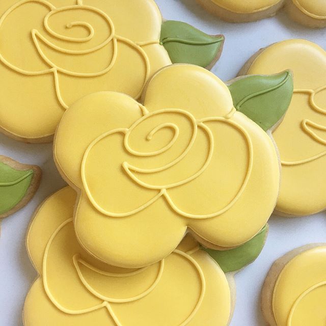 decorated cookies with yellow icing and green leaves on them are arranged in rows, forming the shape of roses