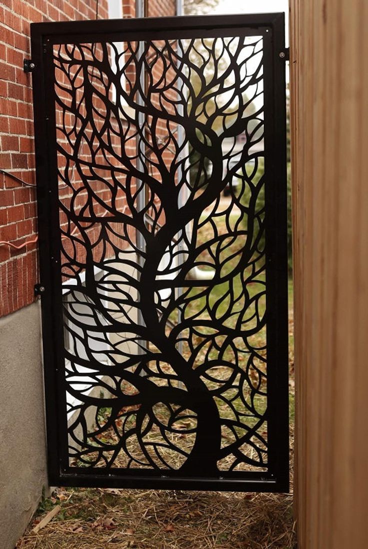 an iron gate with a tree design on the front and back sides, next to a brick wall