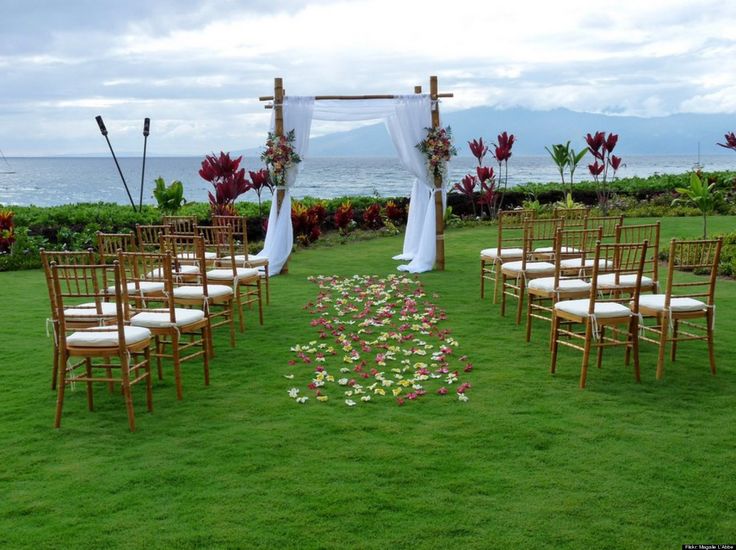 an outdoor ceremony set up with chairs and flowers on the grass by the ocean in hawaii