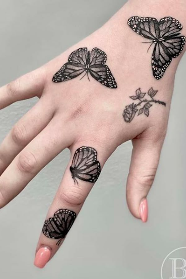 a woman's hand with tattoos on it and four butterflies flying around the fingers