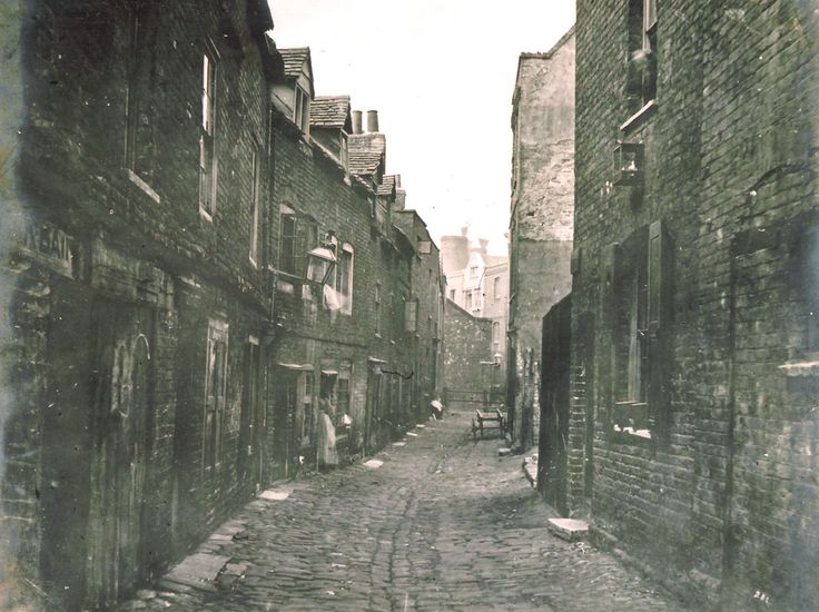 an old photo of people walking down the street in front of brick buildings and cobblestone streets