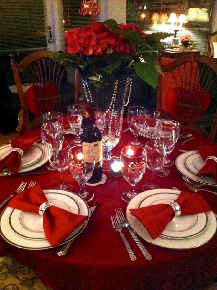 a table set for dinner with red napkins and silverware, wine glasses and candles