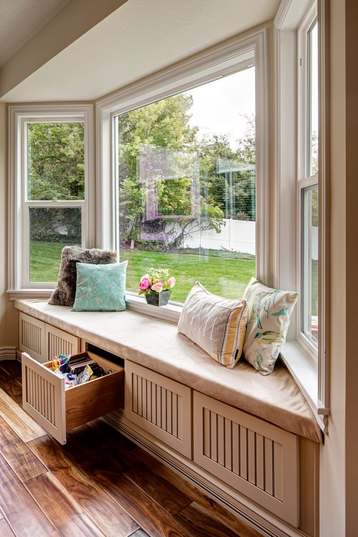 a window seat with pillows on it in front of a large window and wooden floor