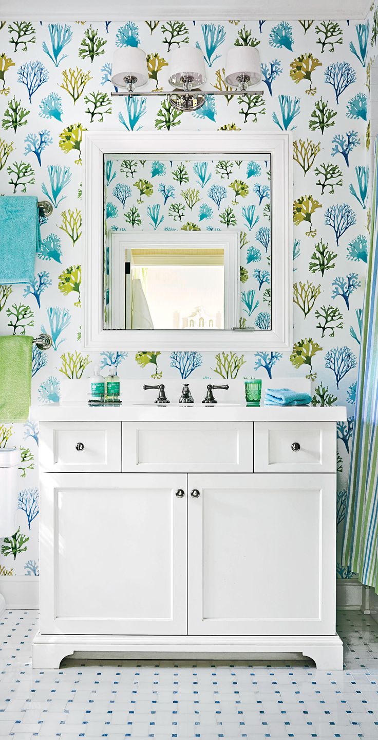 a bathroom with blue and green wallpaper, white cabinets and a large mirror above the sink