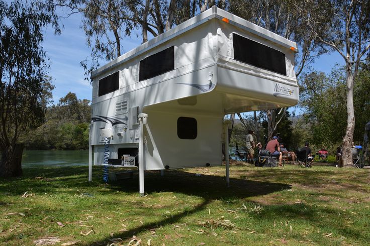 a white trailer sitting on top of a lush green field next to a lake and trees