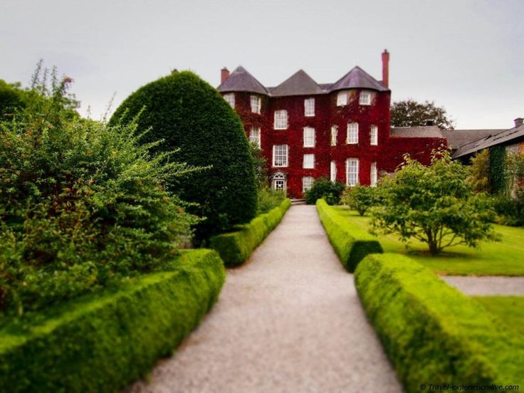 a large red house surrounded by lush green trees and bushes in the foreground is a pathway leading to it