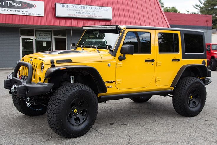 a bright yellow jeep is parked in front of a red and gray building with black tires