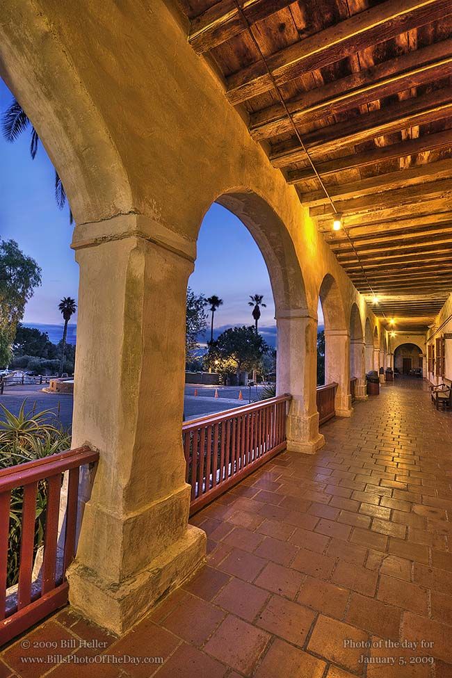 an outdoor covered walkway with arches and benches at night, overlooking the ocean in the distance