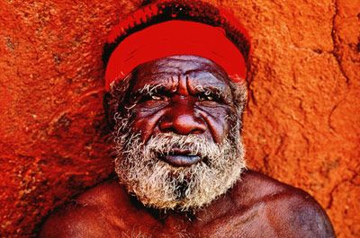 an old man wearing a red hat and standing in front of a wall