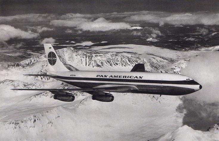 an airplane flying in the sky over some snow covered mountains and clouds on a cloudy day