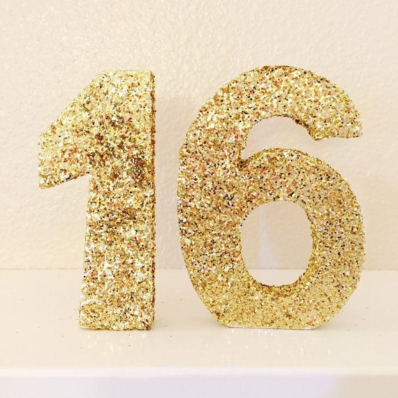 the number sixteen is made out of gold glitters and sits on a white surface