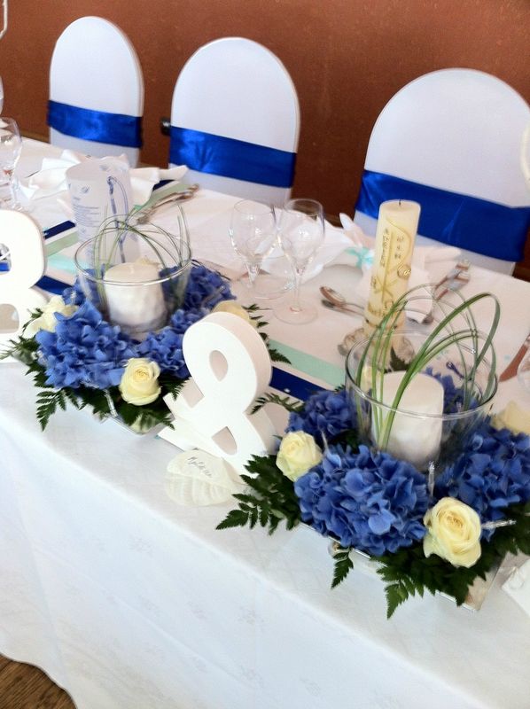 the table is set with blue and white flowers, candles, and numbers on it