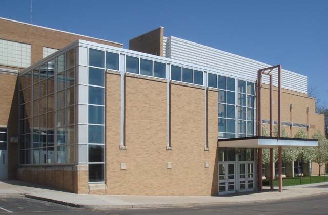 an empty street in front of a brick building with glass windows on the side and a parking lot next to it