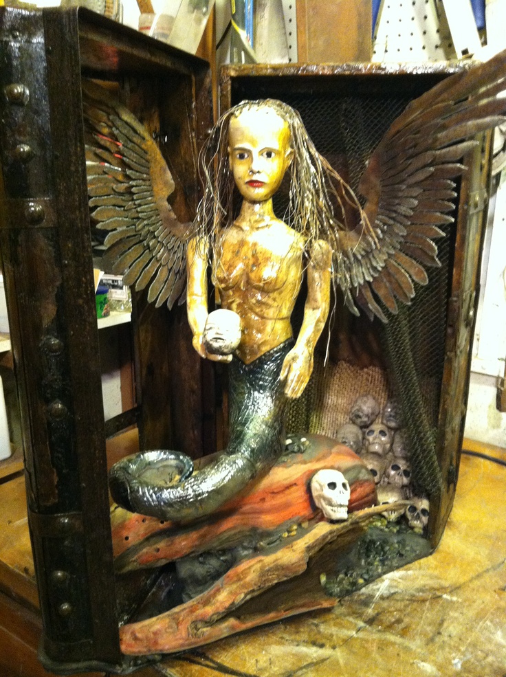 a statue of a mermaid holding a ball in her hands and wings on top of a piece of wood