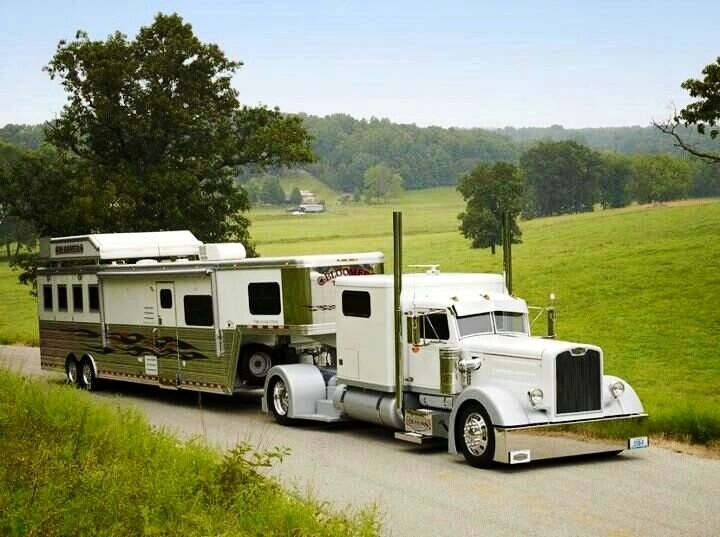 a large white truck pulling a camper trailer down a road in front of a green field