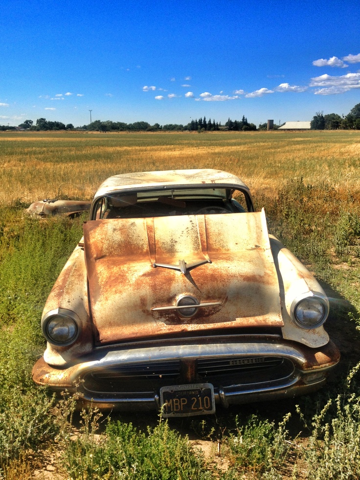 an old rusted car sitting in the middle of a field