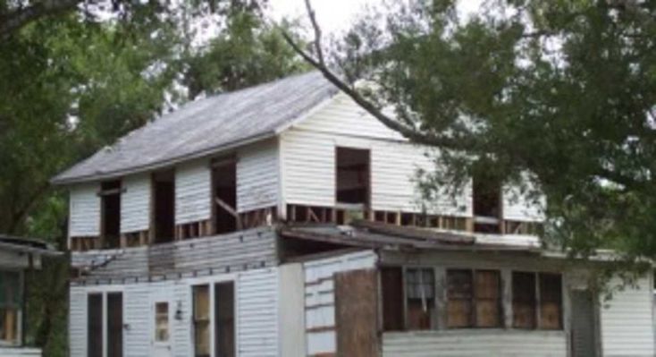 an old white house sitting in the middle of some trees