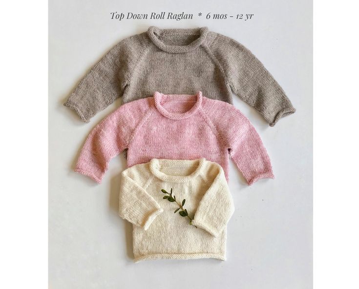 three sweaters are laid out on a white surface, one is pink and the other is grey