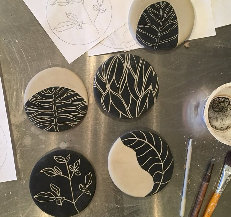 four black and white plates sitting on top of a metal table next to paintbrushes