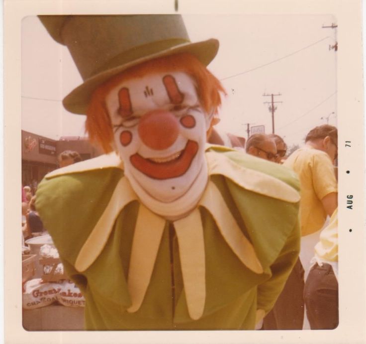 a clown dressed in green and yellow with a hat on his head, standing next to other people