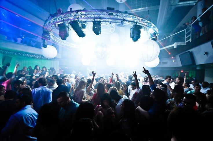 a large group of people at a party with their hands in the air and lights on