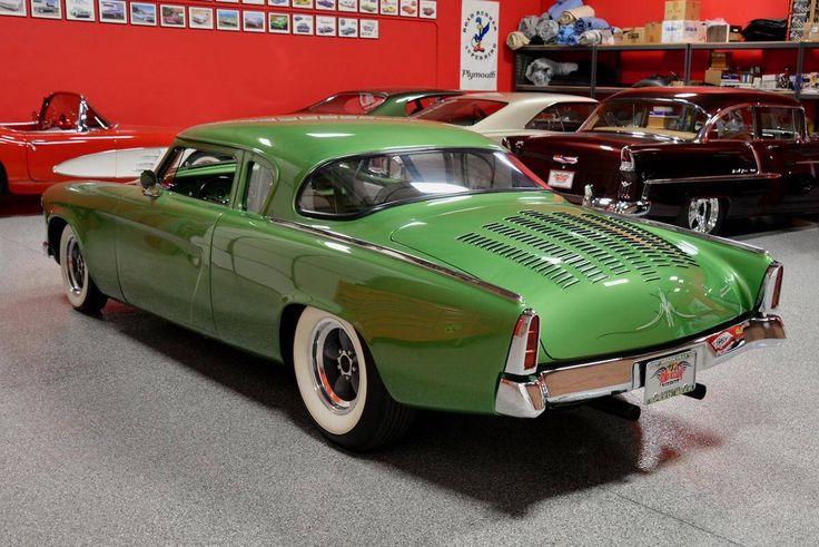 an old green car is parked in a showroom with other classic cars behind it