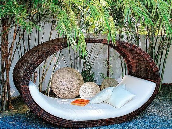 a wicker hammock with two balls and pillows on it in front of a tree