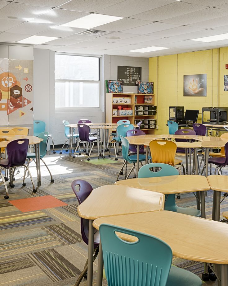 a classroom filled with lots of desks and chairs in front of a book shelf