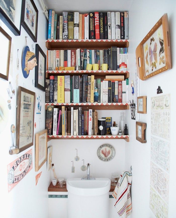 a toilet sitting under a shelf filled with books next to a wall full of pictures