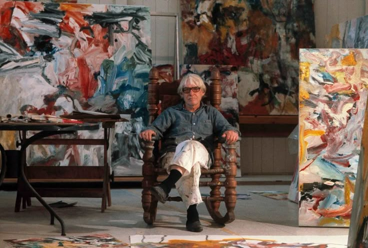 an older man sitting in a chair next to paintings