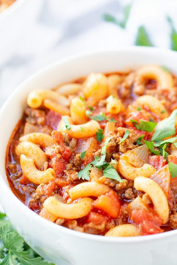 a white bowl filled with pasta and meat sauce on top of a green leafy table