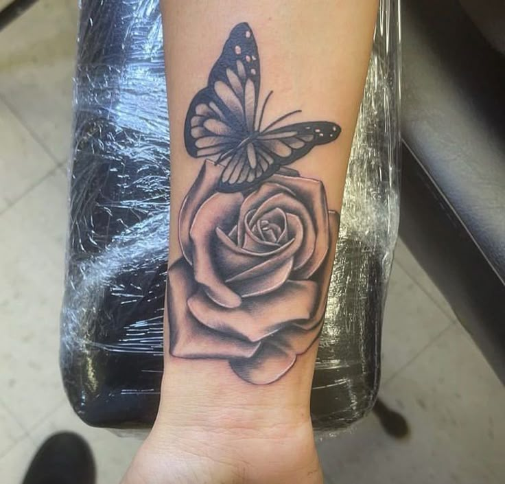 a black and white rose tattoo with a butterfly on it's wrist, in front of a chair