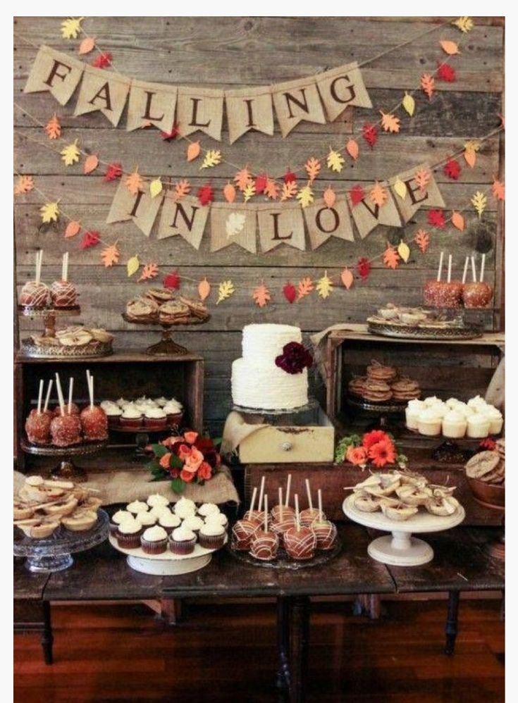 a dessert table filled with cakes and cupcakes on top of wooden tables covered in fall leaves