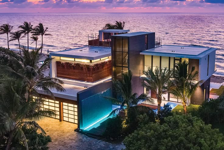 an aerial view of a house on the beach at sunset with palm trees and ocean in the background