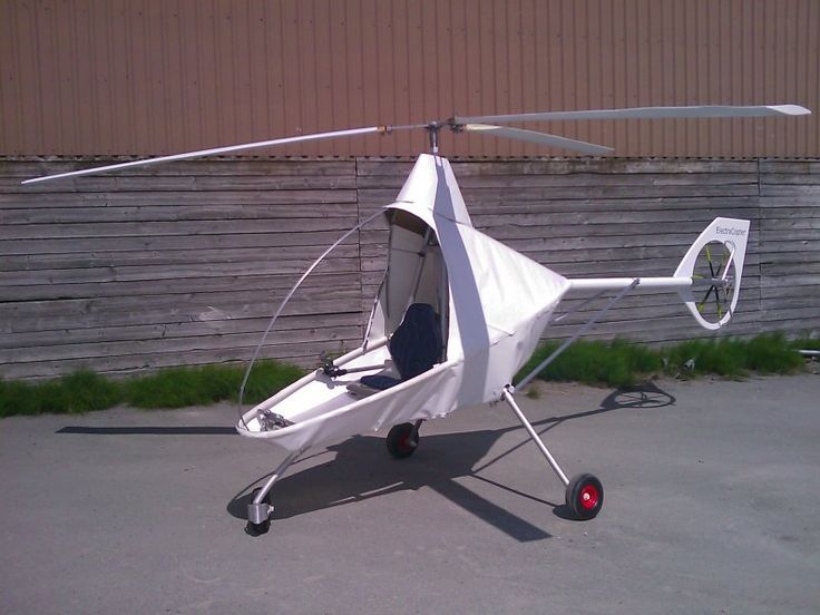 a small white helicopter sitting on top of a parking lot next to a wooden fence