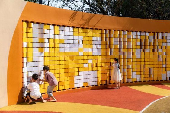 three children are playing on a basketball court with an orange and white wall behind them