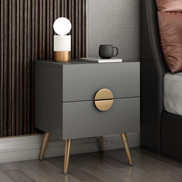 a nightstand with two drawers in front of a bed and pillows on the wall behind it