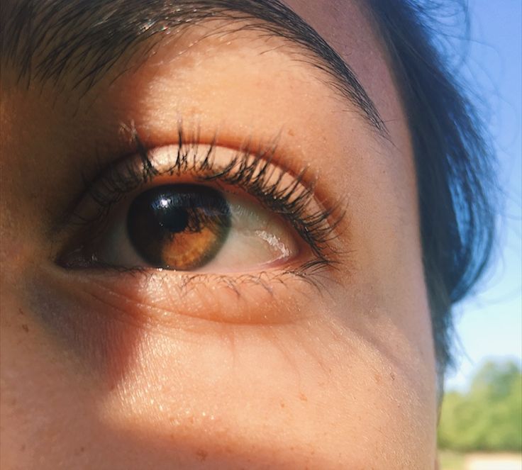 a woman's brown eye with long lashes and blue sky in the back ground