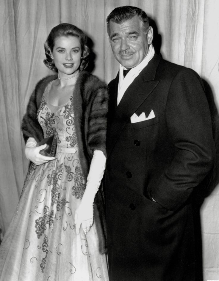 an old black and white photo of two people dressed in formal wear standing next to each other